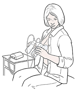 Woman sitting in chair expressing milk from both breasts with electric double breast pump.