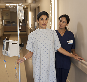 Woman patient walking in hospital hall with an IV pole and nurse.
