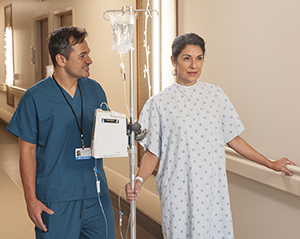 Paciente mujer que camina por el pasillo de un hospital con un soporte IV junto a un enfermero.