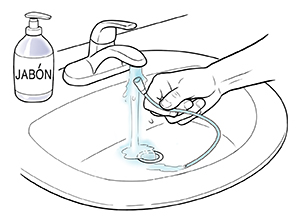 Manos que sostienen una sonda debajo de un chorro de agua en el lavabo. Junto al lavabo, puede verse un recipiente de jabón líquido.