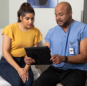 Un proveedor de atención médica y una mujer mirando una tableta electrónica en una sala de examinación.